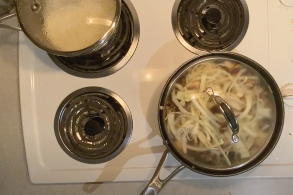 image of two cooking pots on top of a stove. one with boiling rice and the second with boiling evgetable - cabbage and greens,