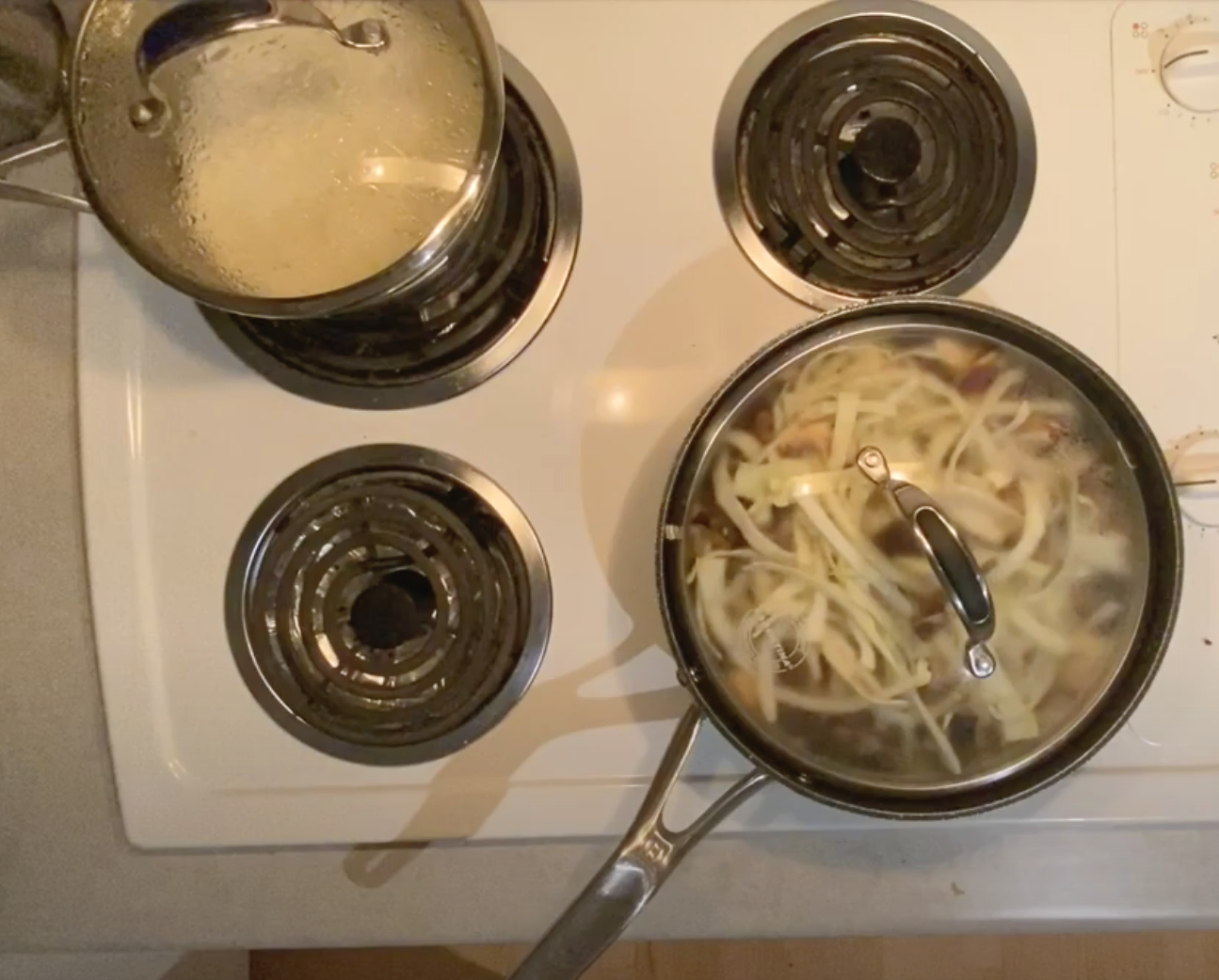 image of two cooking pots on top of a stove. one with boiling rice and the second with boiling evgetable - cabbage and greens,