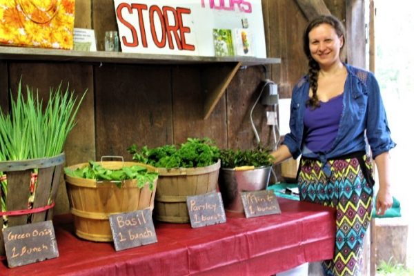 woman standing in front of a table with many vegetables on it for sale at the farm market