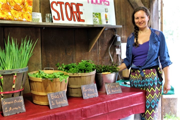 woman standing in front of a table with many vegetables on it for sale at the farm market